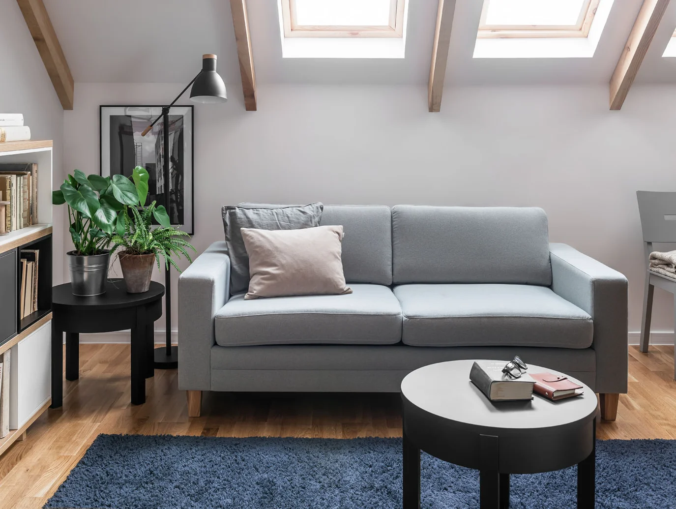 Szara sofa w pokoju na poddaszu z oknami dachowymi i roślinami zapewnia efekt przestrzeni i światła.